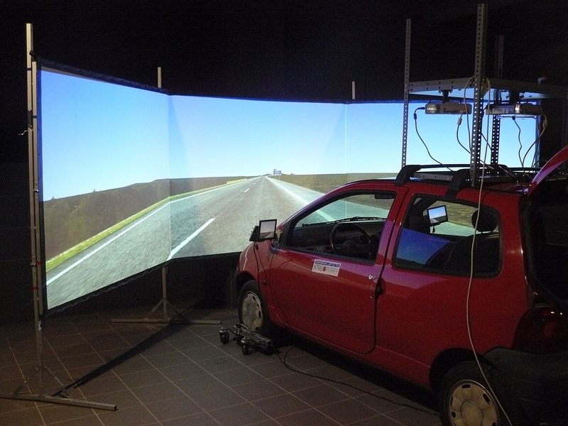 A full-motion sim racing rig facing a large race screen